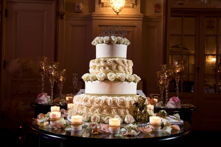 Three-tier wedding cake adorned with floral decorations and candles on a table.