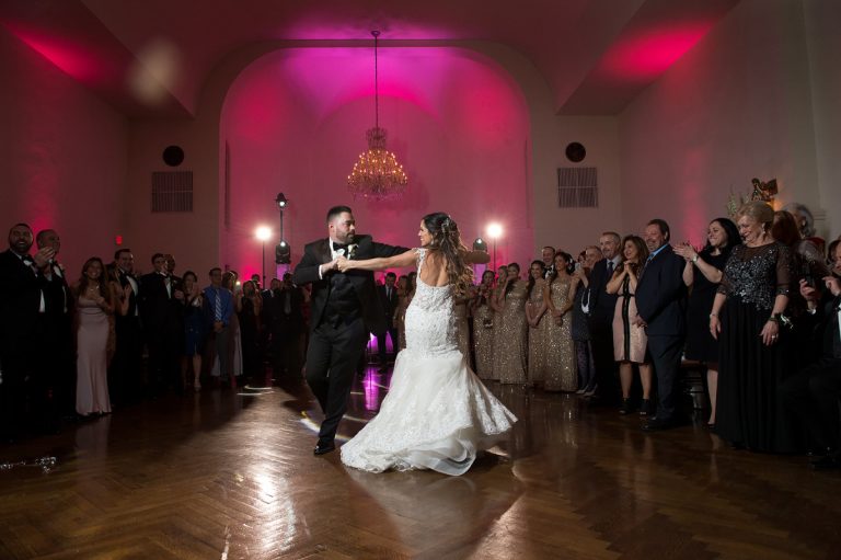 A couple performing their first dance at a wedding reception with guests watching in a decorated venue.
