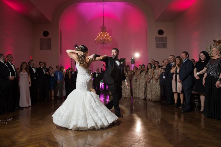 Couple dancing during their first dance at a wedding reception with guests watching in the background.