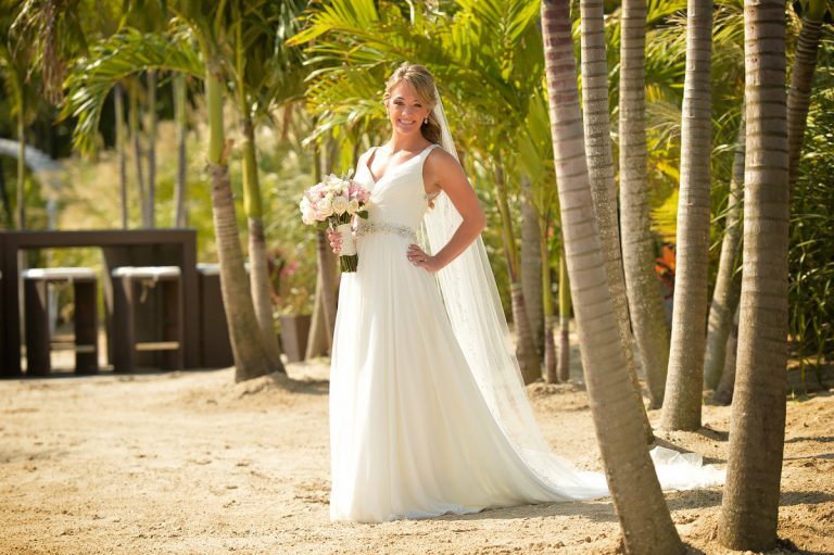 Bride wearing a white wedding dress and holding a bouquet of flowers in a garden setting.