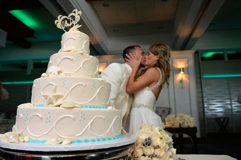 A wedding cake with decorative waves and seashells, alongside a couple sharing a kiss at their wedding reception.