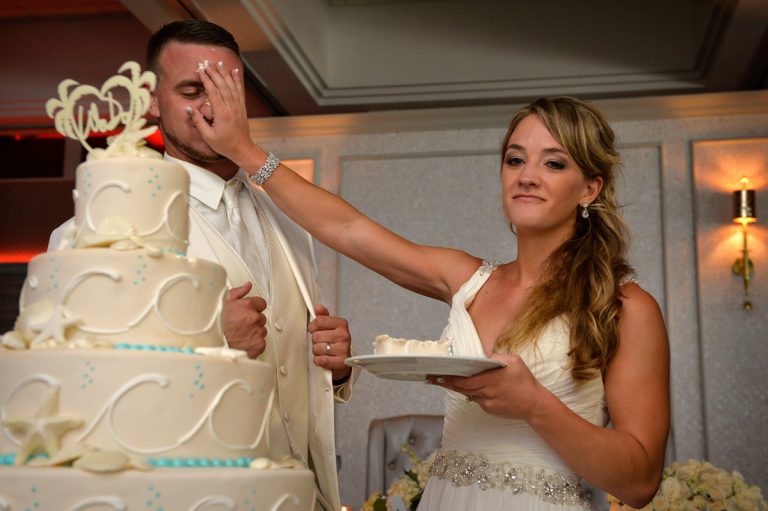 Bride playfully smearing cake on groom's face during a wedding celebration at Crescent Beach Club.
