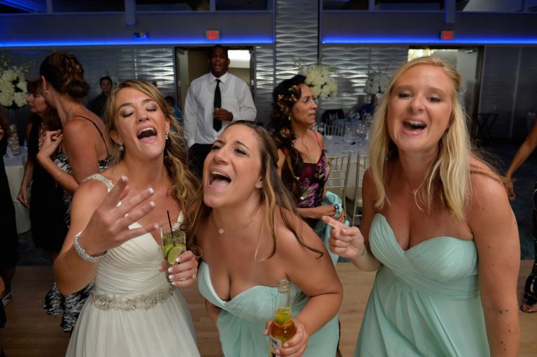 Three women in light blue dresses enjoying a lively moment during a wedding reception.