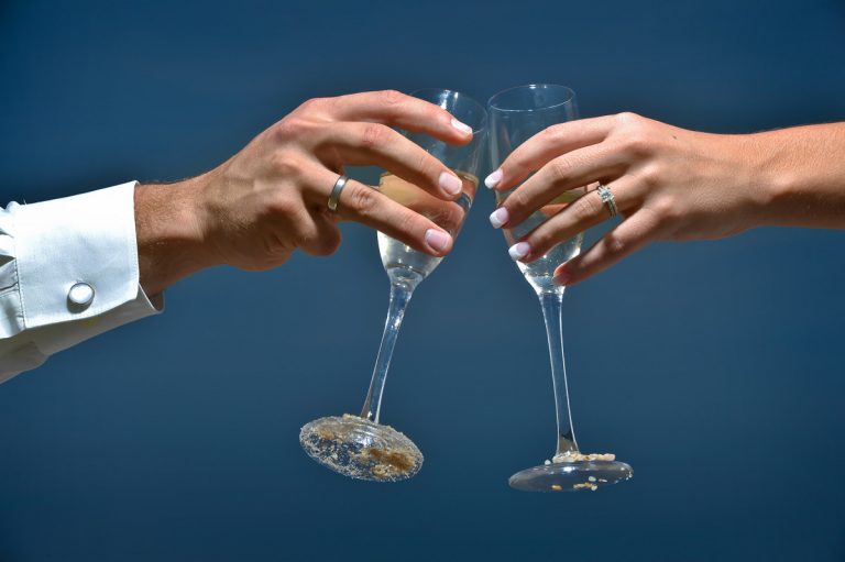 Two hands holding champagne flutes in a toast, both adorned with wedding rings.