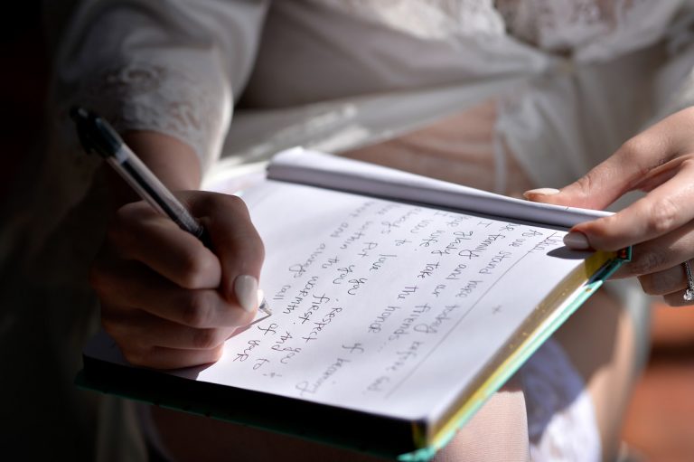 A bride writing a letter on a notepad with a pen, wearing a lace robe.