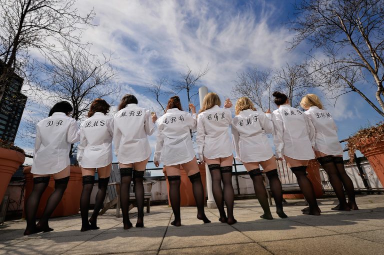 Group of bridesmaids wearing personalized shirts and stockings, posing with their backs to the camera.