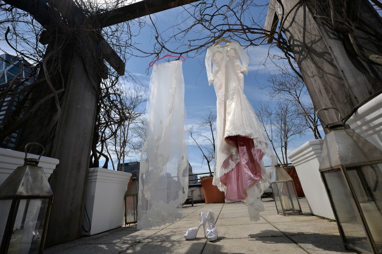 Two wedding dresses hanging on a display outdoors with a clear sky in the background.