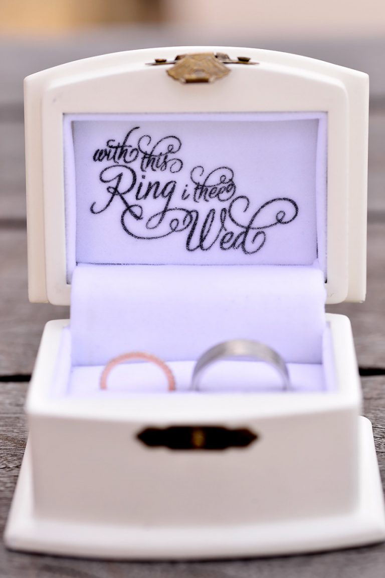 Two wedding rings displayed in a decorative box with a handwritten inscription inside.