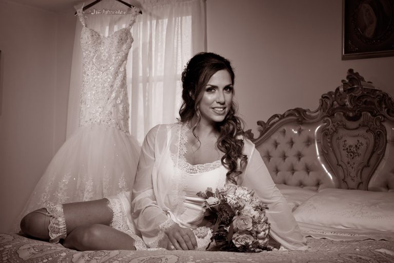Bride posing in a boudoir setting with a wedding dress hanging in the background.