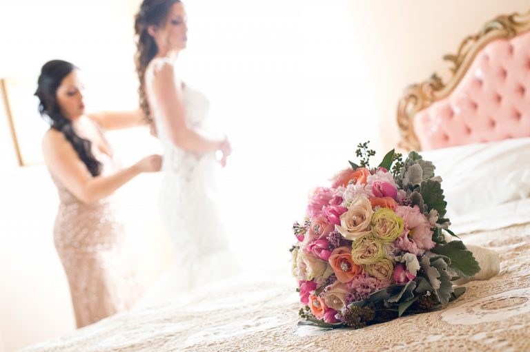 A bride adjusting her dress while holding a colorful bouquet of flowers in the foreground.