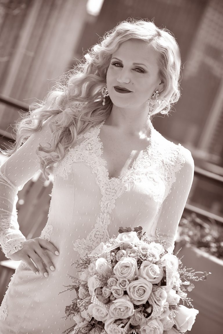 Bride with long blonde hair wearing a white dress and holding a bouquet of roses in New York City.