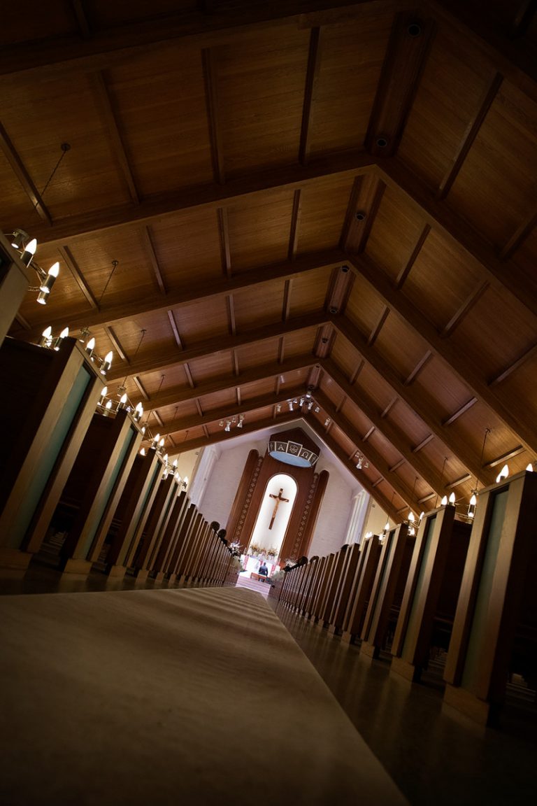 Interior view of a church aisle featuring a wooden ceiling and a cross at the altar.