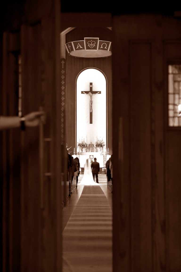 A couple walking down the aisle during a wedding ceremony inside a church with a cross in the background.