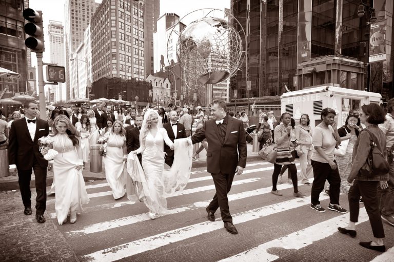 Bride and groom walking together across a busy street at Columbus Circle with a globe sculpture in the background.