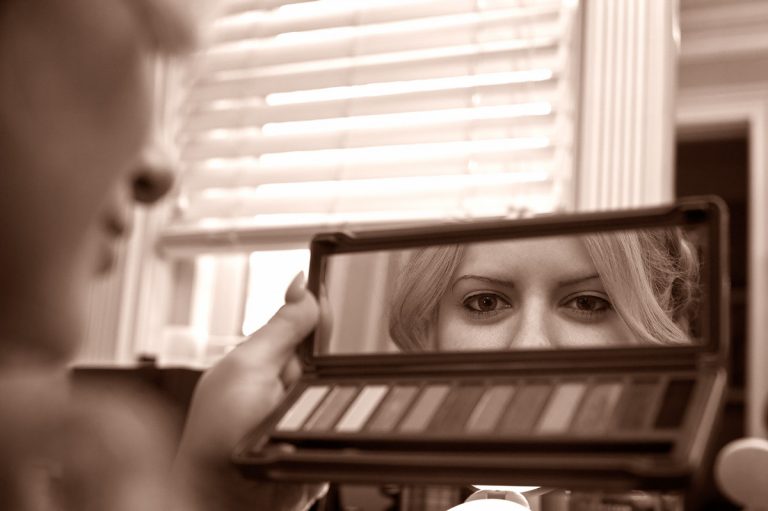 A person holding a makeup palette in front of a mirror, reflecting their eyes.