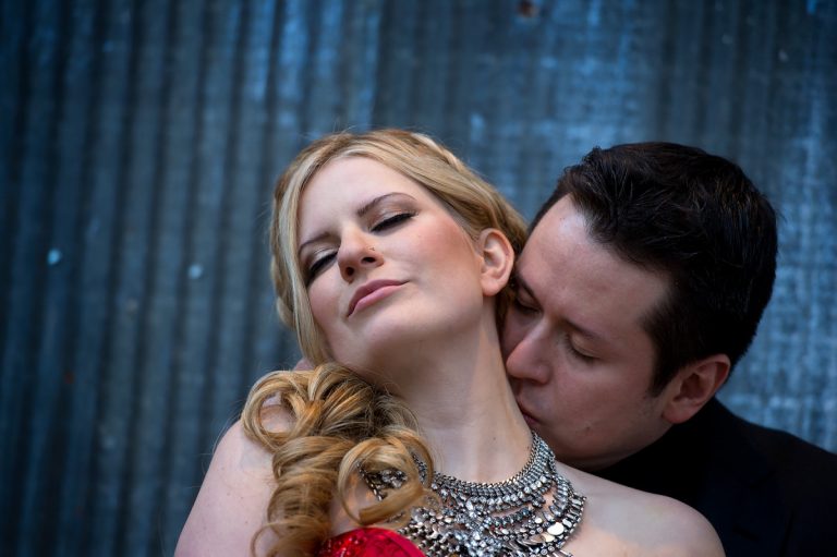 A couple in an intimate embrace, with the man kissing the woman's neck while she closes her eyes.