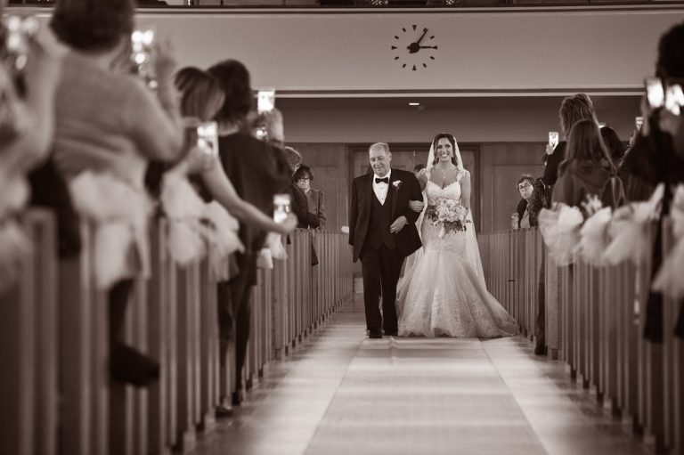 A bride in a wedding dress walking down the aisle with her father during a ceremony.