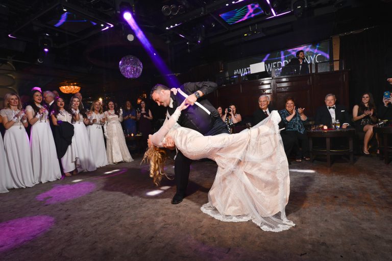 A couple performing a dance during their wedding reception with guests watching in formal attire.