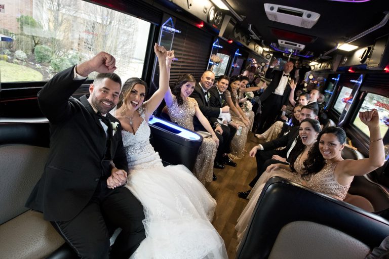 Bridal party celebrating inside a party bus with raised hands and joyful expressions.