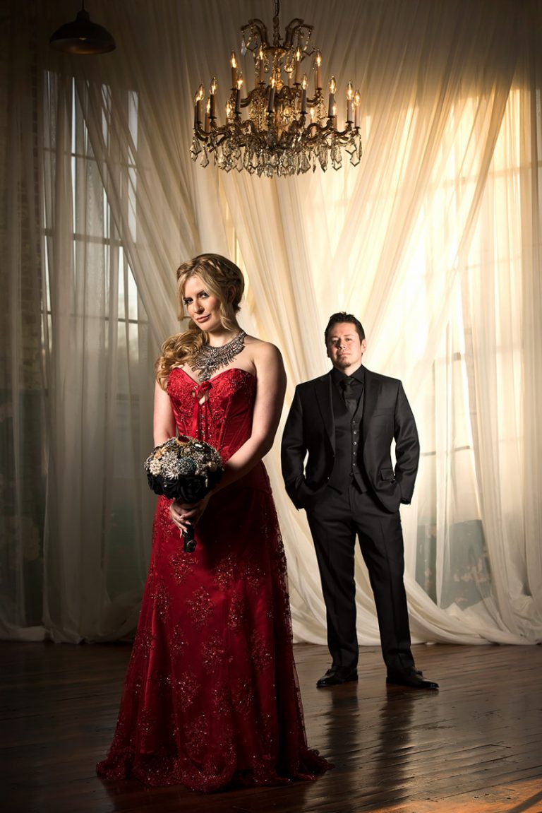 Bride wearing a red wedding dress holding a bouquet, standing next to a groom in a black suit.