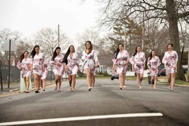 Group of bridesmaids wearing matching pink floral robes walking together on a street.