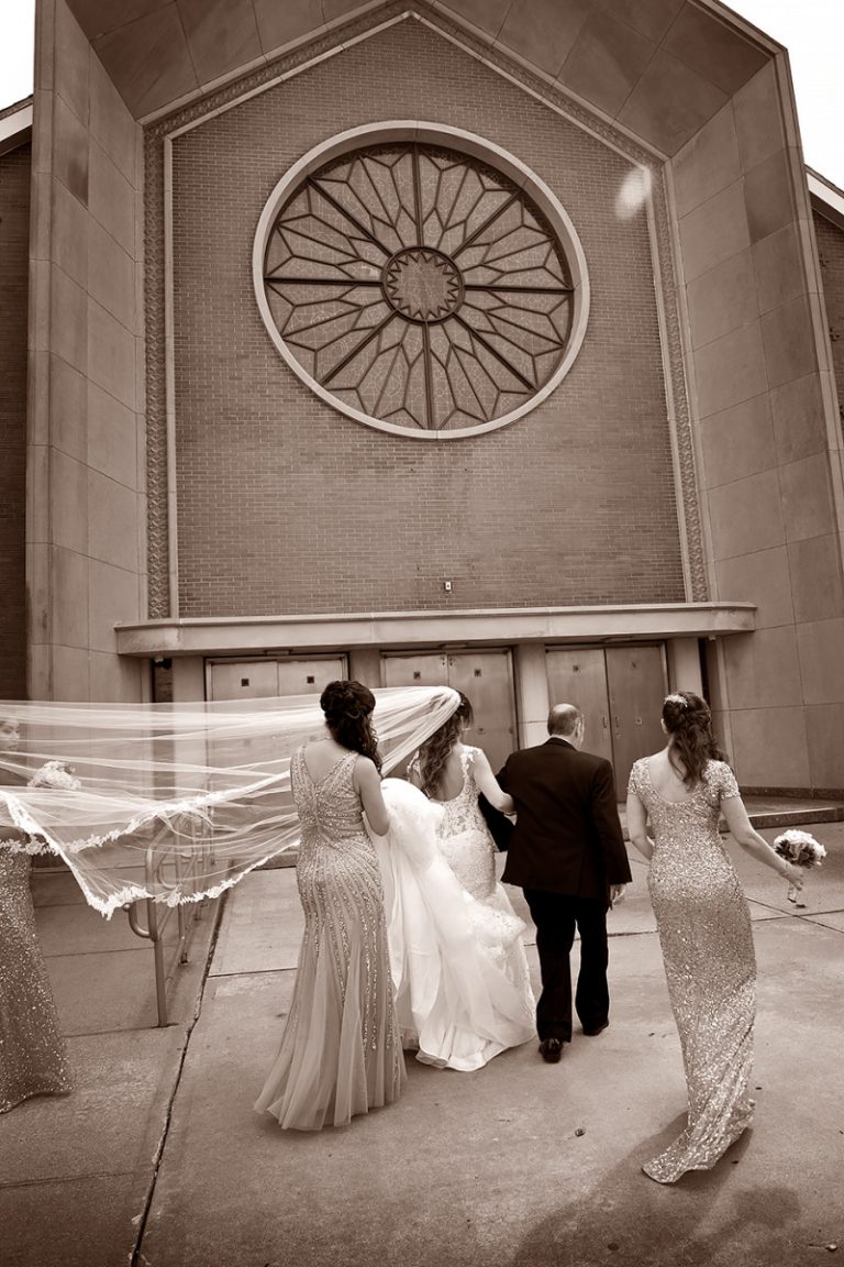 Group of individuals walking towards a church with a large circular window in the background.