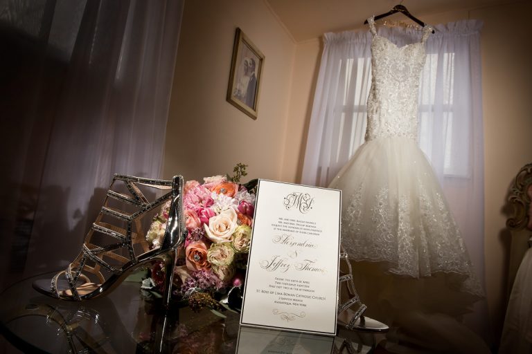 A wedding dress hanging beside a bouquet and an invitation on a table.