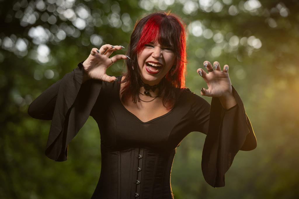 A woman with red and black hair wearing a black dress, playfully posing with a fierce expression.