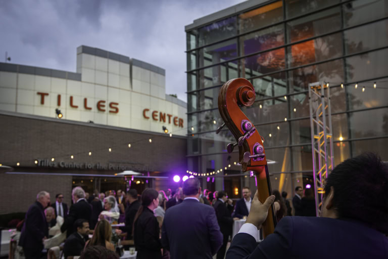 Close-up of a double bass being played at an outdoor event in front of the Tilles Center for the Performing Arts.