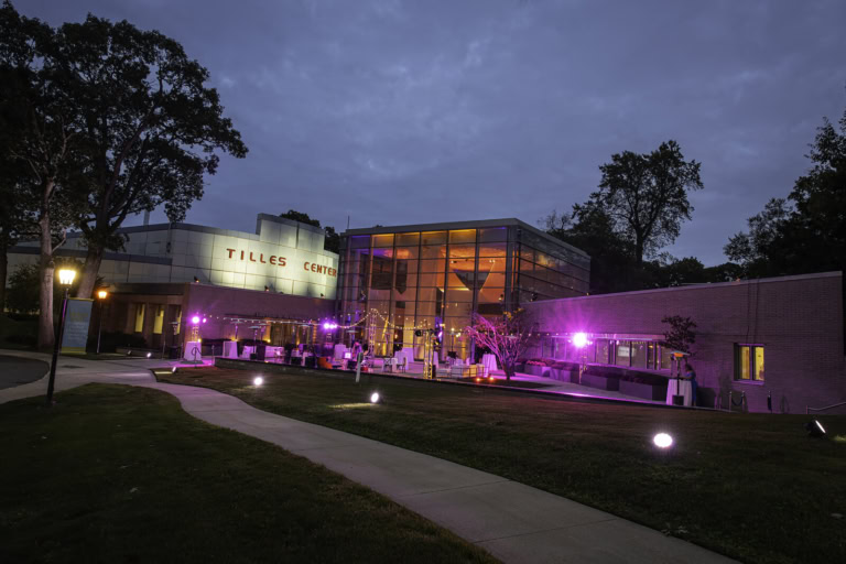 Tilles Center building illuminated with purple lights during twilight, showcasing modern architecture and landscaped grounds.