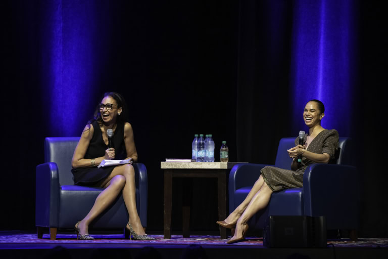 Misty Copeland seated on stage, laughing and engaging in conversation, with microphones in hand and water bottles on a table at Tilles Center