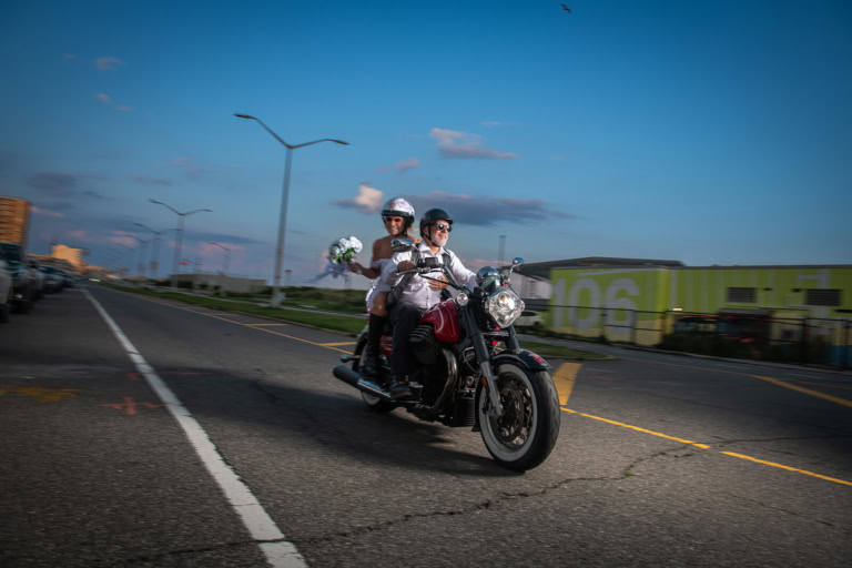 A couple rides a black motorcycle along a divided urban highway as evening light falls across the roadway.
